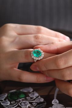 a woman's hand holding a ring with an emerald and diamond center in it