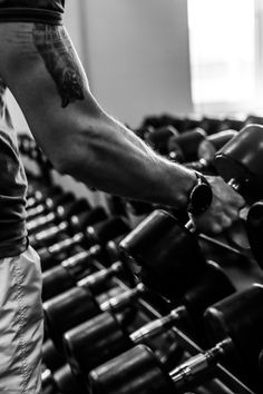 black and white photograph of a man with his arm wrapped around dumbbells in a gym