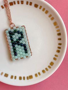 a white plate topped with a blue and green beaded square pendant on a chain