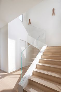 a staircase with glass railing and wooden handrails in a white room next to an open door