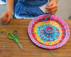 a child is making a paper plate craft with scissors and thread on the table next to it