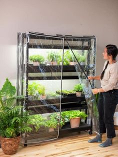 a woman standing in front of a greenhouse with plants growing on it's sides