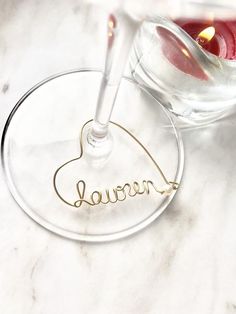 a wine glass with the word lauren written in cursive writing on it, next to a candle