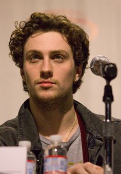 a young man with curly hair sitting in front of a microphone and looking at the camera