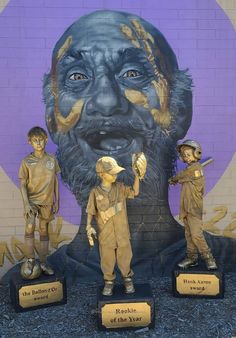 three statues of children standing in front of a wall with an image of a man's face on it