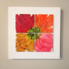 four different colored flowers on a white square wall mounted in a room with beige walls