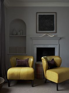 a magazine with two yellow chairs in front of a fire place and a painting on the wall