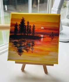 an easel with a painting on it sitting in front of a window at sunset