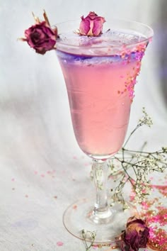 a pink cocktail in a glass with flowers on the rim