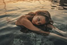 a woman laying on top of a rock in the middle of some water at sunset