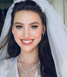 a woman wearing a wedding veil and smiling at the camera with her hair pulled back