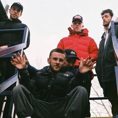 a group of men sitting next to each other in front of a metal structure with their hands up