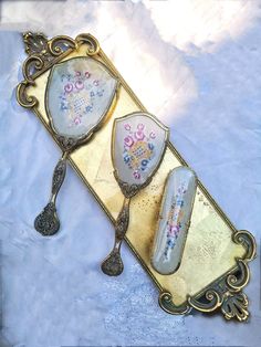 an ornate mirror with two spoons in it on top of a white table cloth