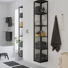 a white bathroom with black shelving and towels on the shelves, along with a potted plant