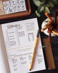 an open planner and some pencils on a wooden table next to a potted plant