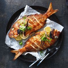 two fish on a plate with lemon slices and garnished with green onions, served with silverware