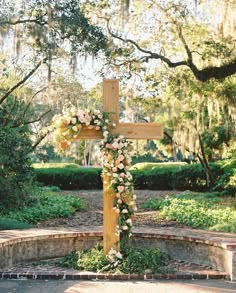 a wooden cross with flowers on it sitting in the middle of a park surrounded by trees