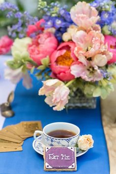 a cup of tea on a blue table cloth with flowers in vases behind it