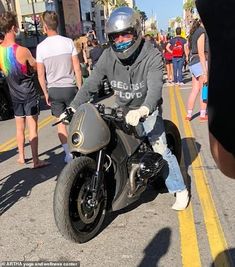 a man riding on the back of a motorcycle down a street next to other people