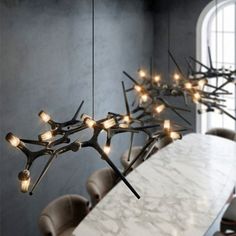 an artistic chandelier hangs over a dining room table with chairs and a white marble top