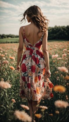 a woman in a dress walking through a field full of flowers with her back to the camera