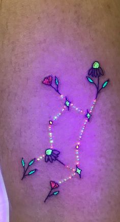 a woman's tattoo with flowers and beads on her stomach that is glowing in the dark