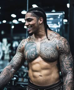 a man with tattoos on his chest standing in front of a gym equipment rack and looking at the camera