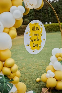 a little honey is on the way sign surrounded by yellow and white balloons in a garden