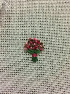 some pink flowers sitting on top of a white cloth covered in green and red thread