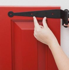 a person's hand is holding the handle on a red cabinet door with black hardware