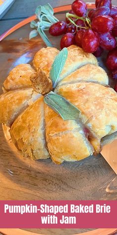 a pumpkin shaped baked brie on a plate next to grapes and a butter knife