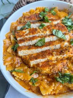 a white plate topped with pasta and meat covered in sauce, garnished with green leaves