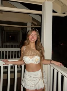 a woman standing on a balcony with her arms out and smiling at the camera while wearing a white skirt