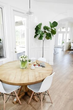 a dining room table with white chairs and a potted plant in the center on top