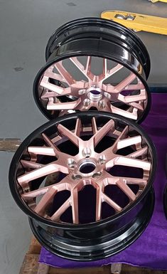 two black rims with pink spokes are sitting on a purple cloth next to each other