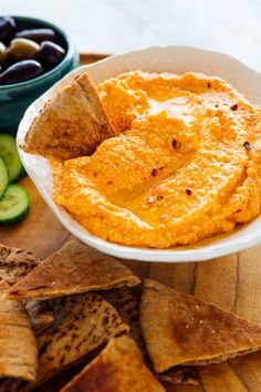 hummus and pita chips on a cutting board with olives, cucumber and pickles