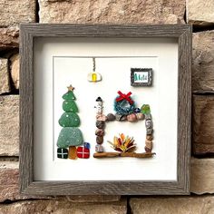 a frame with some christmas decorations hanging on the wall next to a brick wall and a stone wall