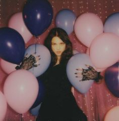 a woman standing in front of balloons with her hands on the ballons behind her