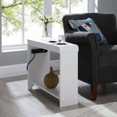 a white table with a vase on it next to a gray chair and window sill