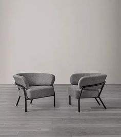 two gray chairs sitting on top of a hard wood floor next to each other in front of a white wall