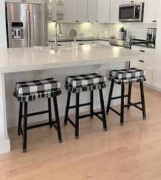 three stools sit at the center of a kitchen island with white cabinets and stainless steel appliances