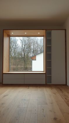 an empty room with wood flooring and large open window overlooking trees outside the window