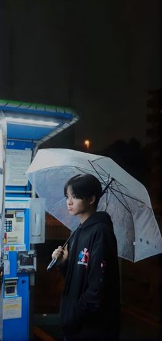 a young man standing next to a vending machine with an umbrella over his head