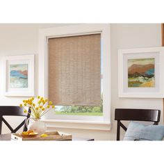 a living room with a window covered in roman shades and yellow flowers on the table