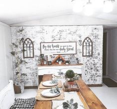 a dining room table set with place settings and plates on it, in front of a brick wall