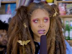 a woman with dreadlocks holding a microphone in front of her face and looking at the camera