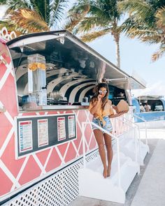 a woman standing on the side of a food truck with palm trees in the background