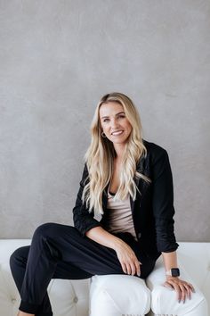 a woman sitting on top of a white couch next to a gray wall and smiling at the camera