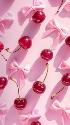 cherries with bows and ribbons are arranged on a pink surface, as if they were made out of candy