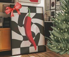 a christmas tree in the corner of a room with pictures on the wall and a red pepper hanging from it